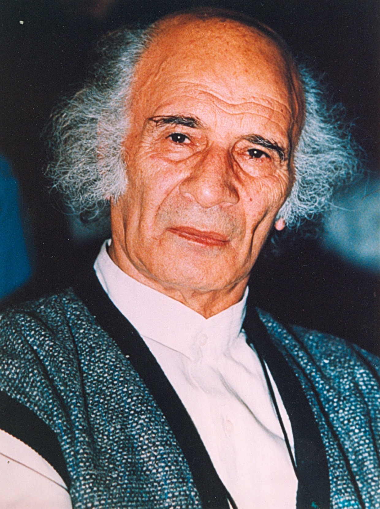 پرترهٔ استاد جلیل ضیاءپور در سالمندی، با پیراهن سفید و ژاکت بافتنی آبی، در زمینهٔ تیره
