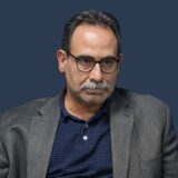 پرترهٔ دکتر حجت امانی با کت خاکستری و پیراهن سرمه‌ای، در برابر زمینهٔ سرمه‌ای