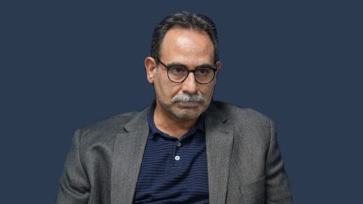 پرترهٔ دکتر حجت امانی با کت خاکستری و پیراهن سرمه‌ای، در برابر زمینهٔ سرمه‌ای