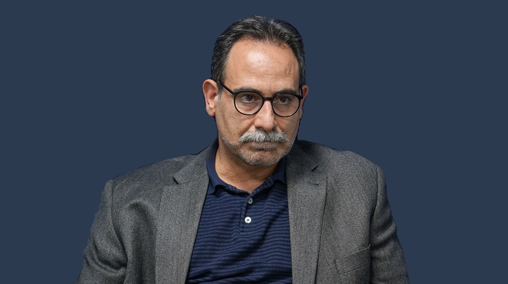 پرترهٔ دکتر حجت امانی با کت خاکستری و پیراهن سرمهای، در برابر زمینهٔ سرمهای